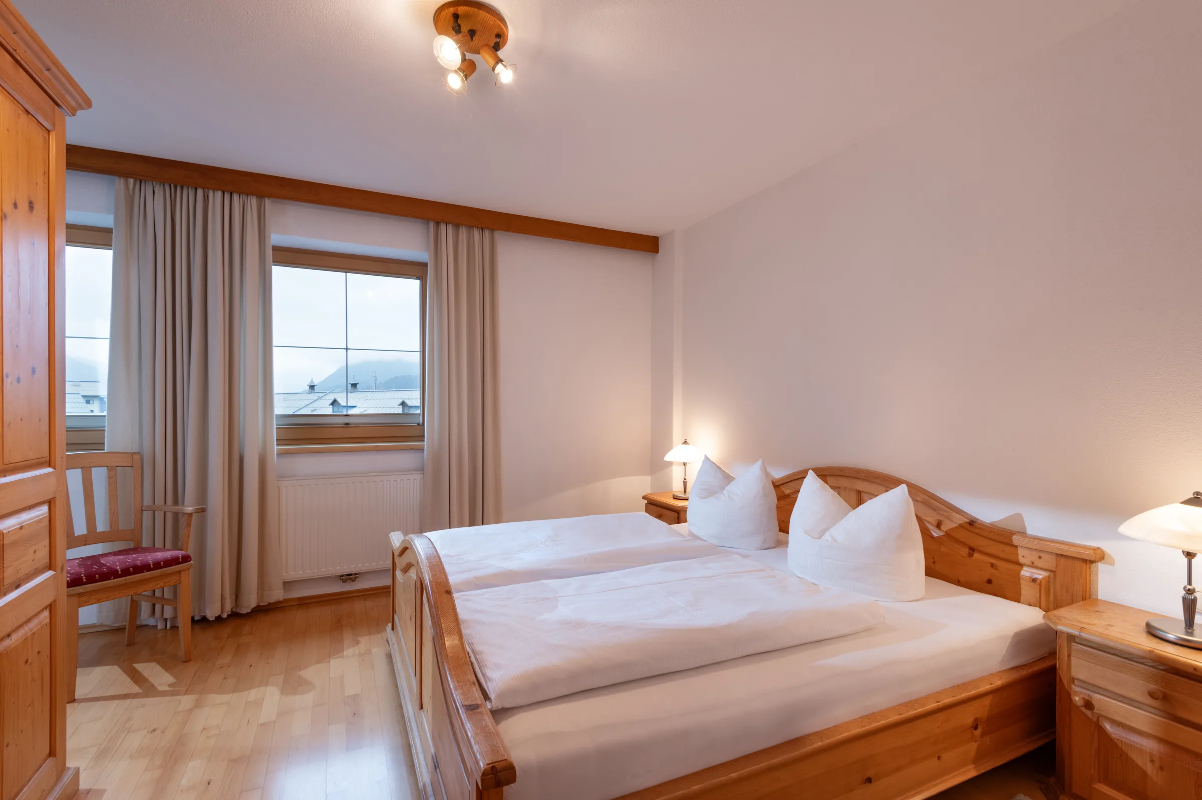 Schlafzimmer mit Doppelbett aus Pinienholz und Bogenfenster, Appartement mit Balkon des Appartement Erler.