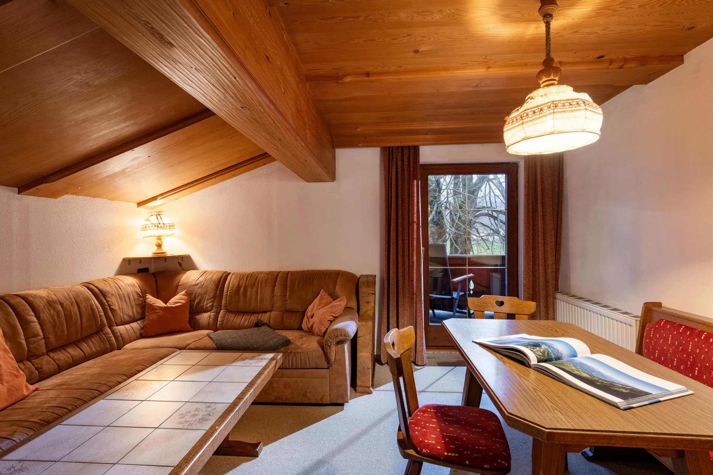 Wohnzimmer mit brauner Ledereck-Couch, gefliestem Couchtisch und Dachschräge aus Pinienholz, Appartement Kitzbüheler Horn am Bauernhof Oberlacken.